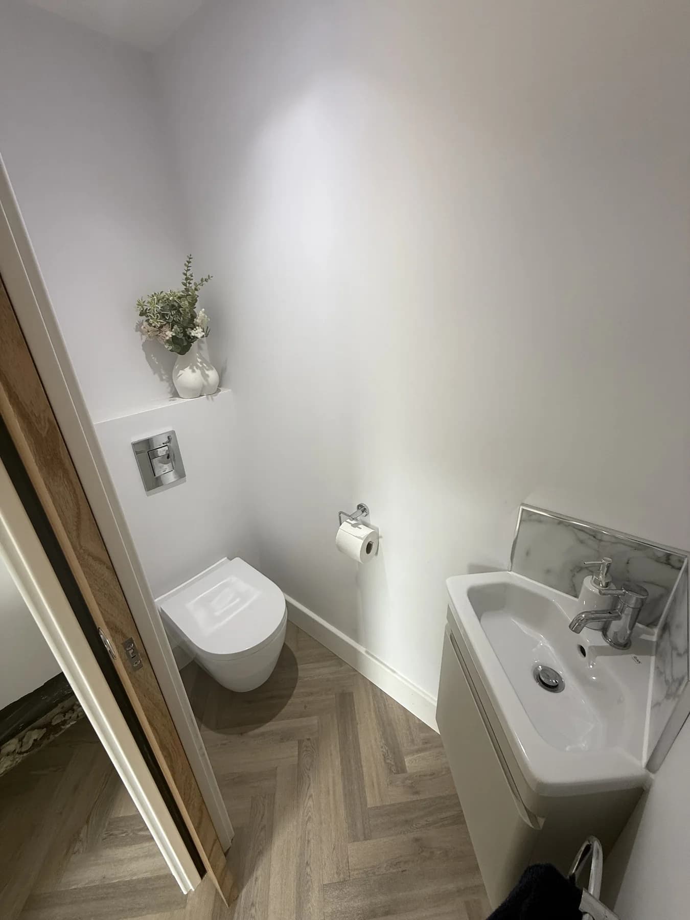 Finished cloakroom with wall-mounted toilet, compact basin and marble-effect splashback